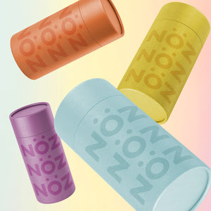 Angled views of 4 canisters of NӦZ sunscreen for the nose in light orange, yellow, purple, and light blue